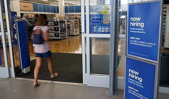 A woman is entering a supermarket which have a "now hiring" notice board in front of the entrance