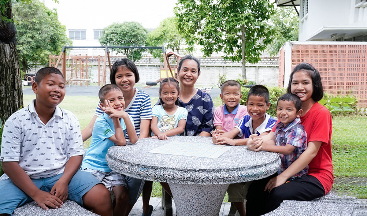 Many Thai children and a teacher is smiling and sitting around the table